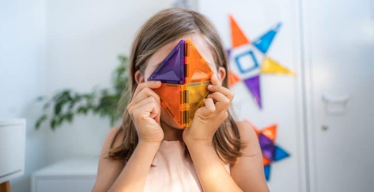 Young girl holding coloured Connetix magnetic tiles over her face