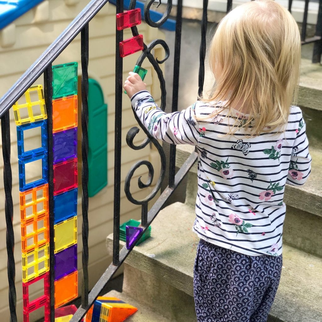 Child playing with Connetix Tiles attached to outdoor metal railing