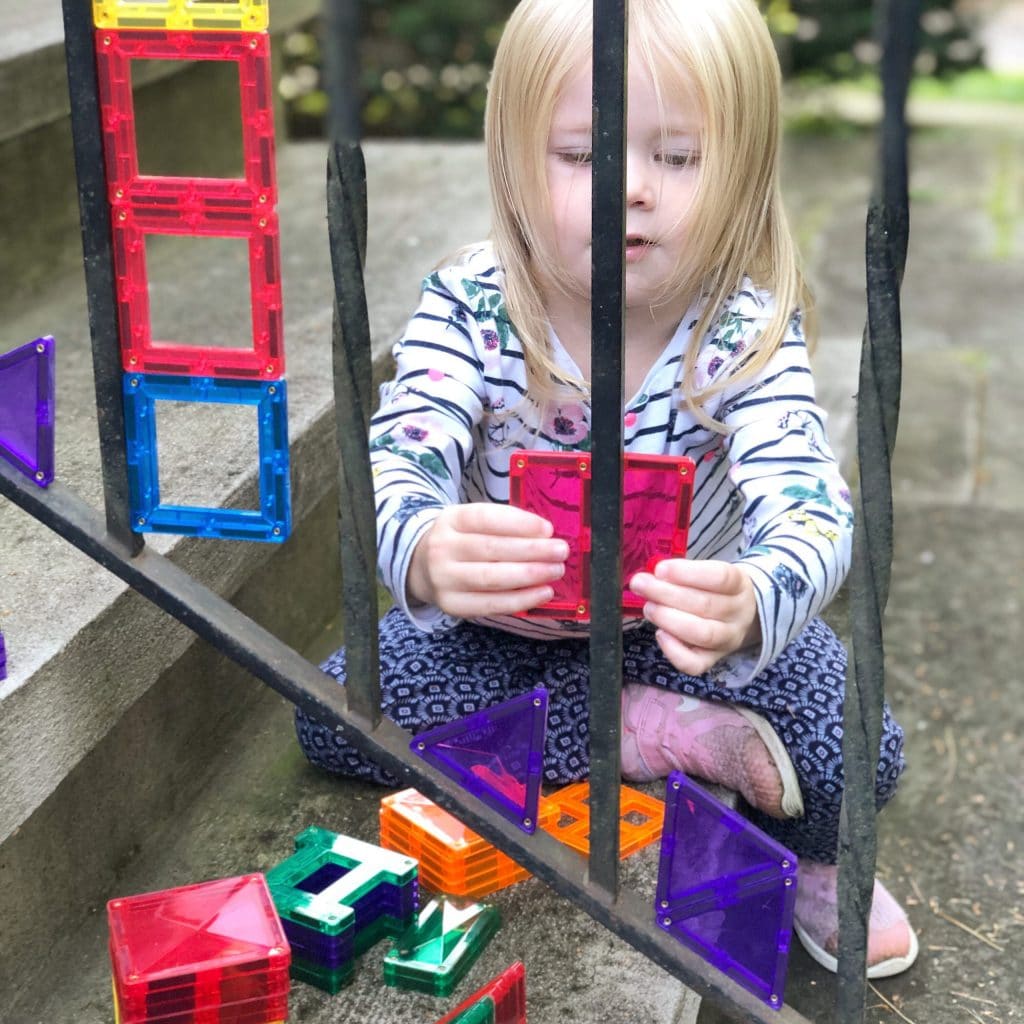 Child playing with Connetix Tiles attached to metal railing